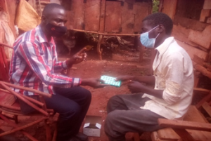 Photo 2: Client (in white long-sleeved shirt) being supported to start TB continuation phase by a health worker from AIC Jinja
